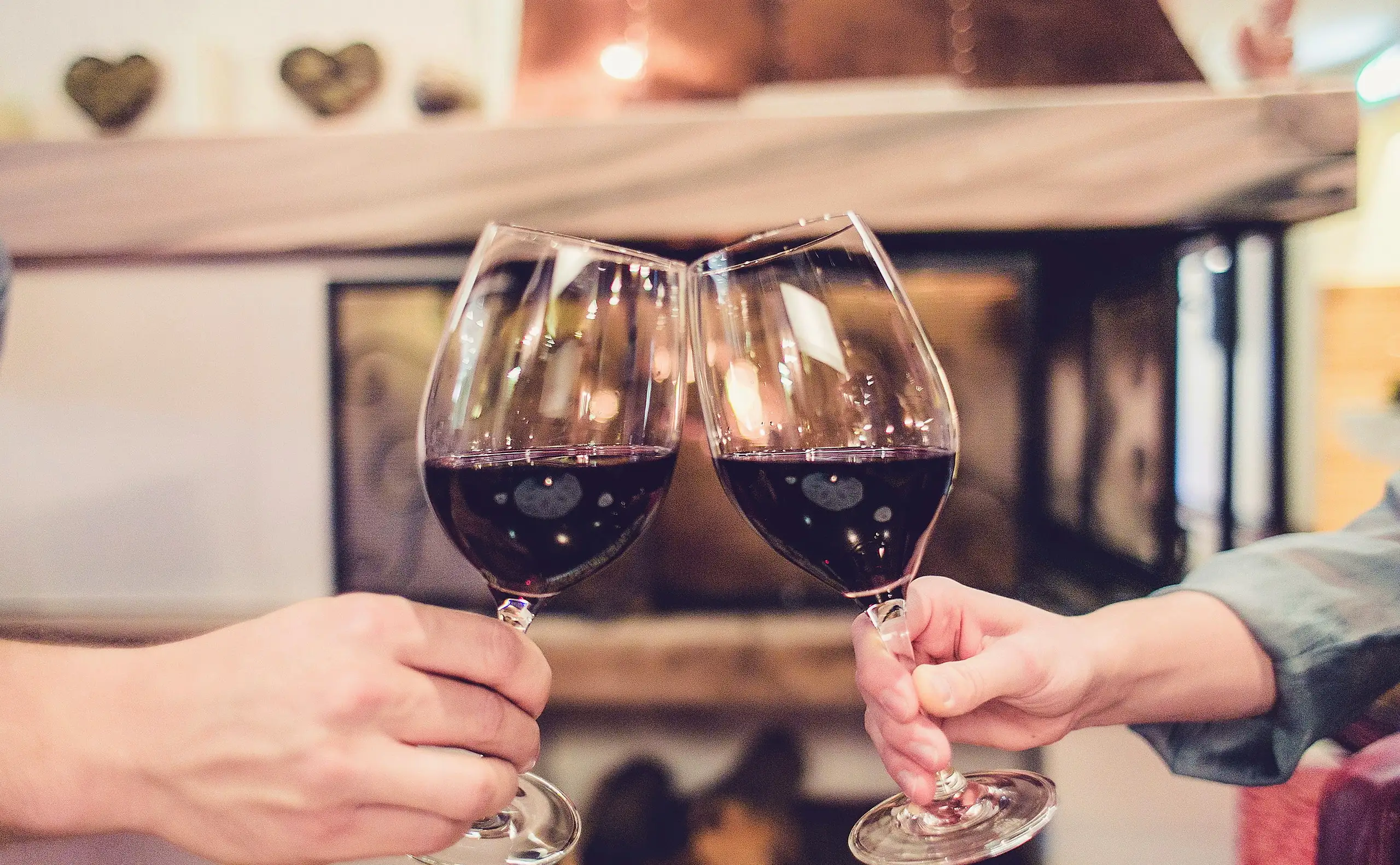 Zwei Gäste stoßen mit Rotwein an, dahinter die Stube des Schlosshotels Seewirt
